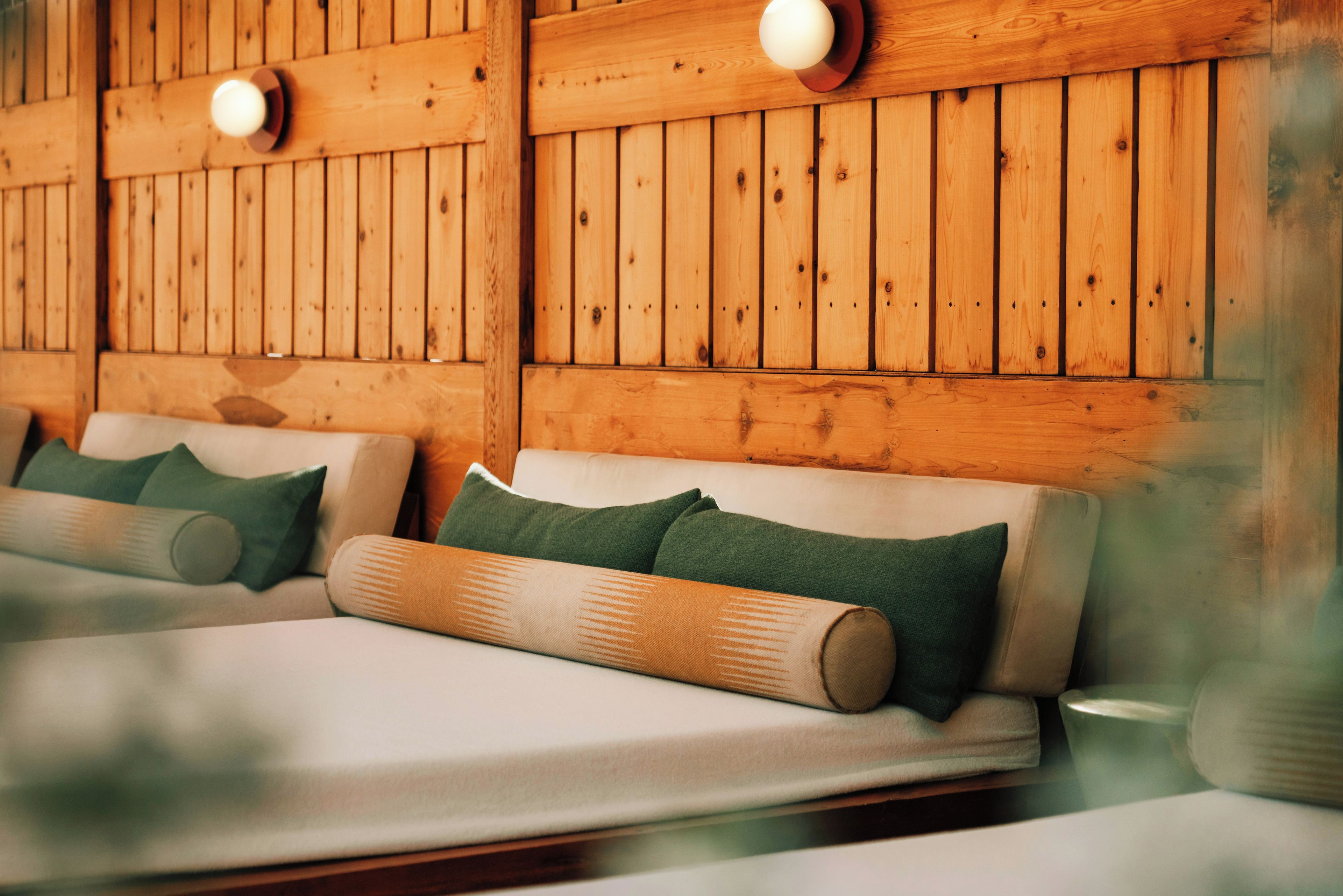 A room with wooden panel walls, two beds with green and beige pillows, and a small table.
