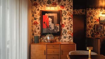 A room with a wooden cabinet, a framed artwork, and a patterned wallpaper.