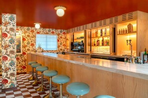 Uma área de bar com banquetas, balcão e prateleiras com garrafas.