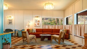 A room with a checkered floor, a sofa, two chairs, a coffee table, and a window with curtains.