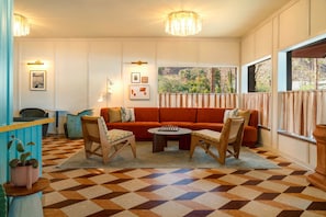 A room with a checkered floor, a sofa, two chairs, a coffee table, and a window with curtains.