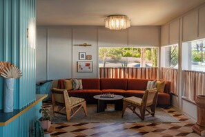 A living room with a red sofa, two armchairs, a coffee table, a chandelier, and a view of the outdoors through large windows.