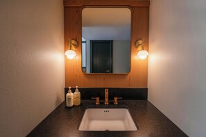 A bathroom with a wooden vanity, a white sink, and two wall-mounted lights. - Royal Sun Palm Springs (Palm Springs)