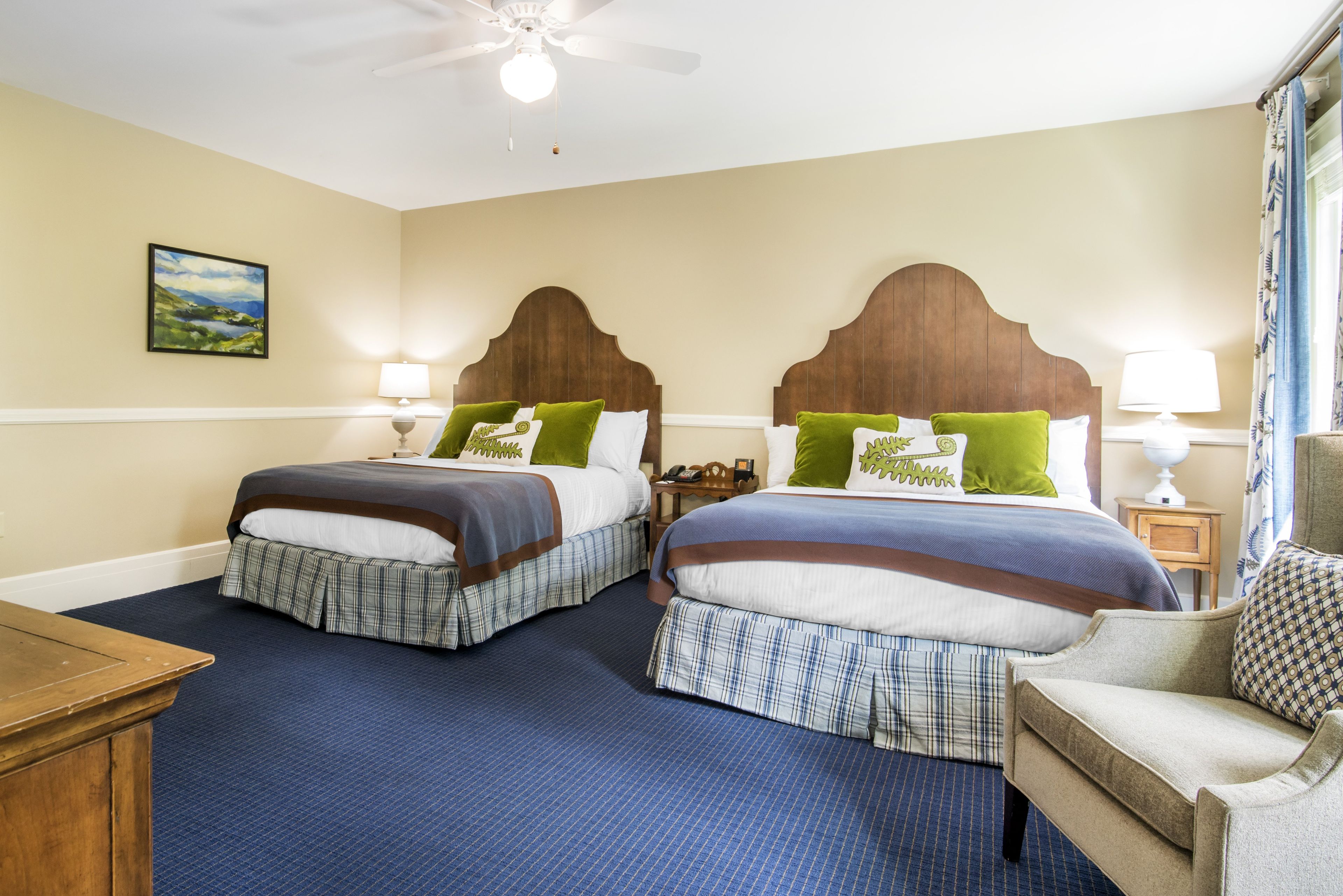 A hotel room with two beds, a wooden headboard, a painting on the wall, and a blue carpet.