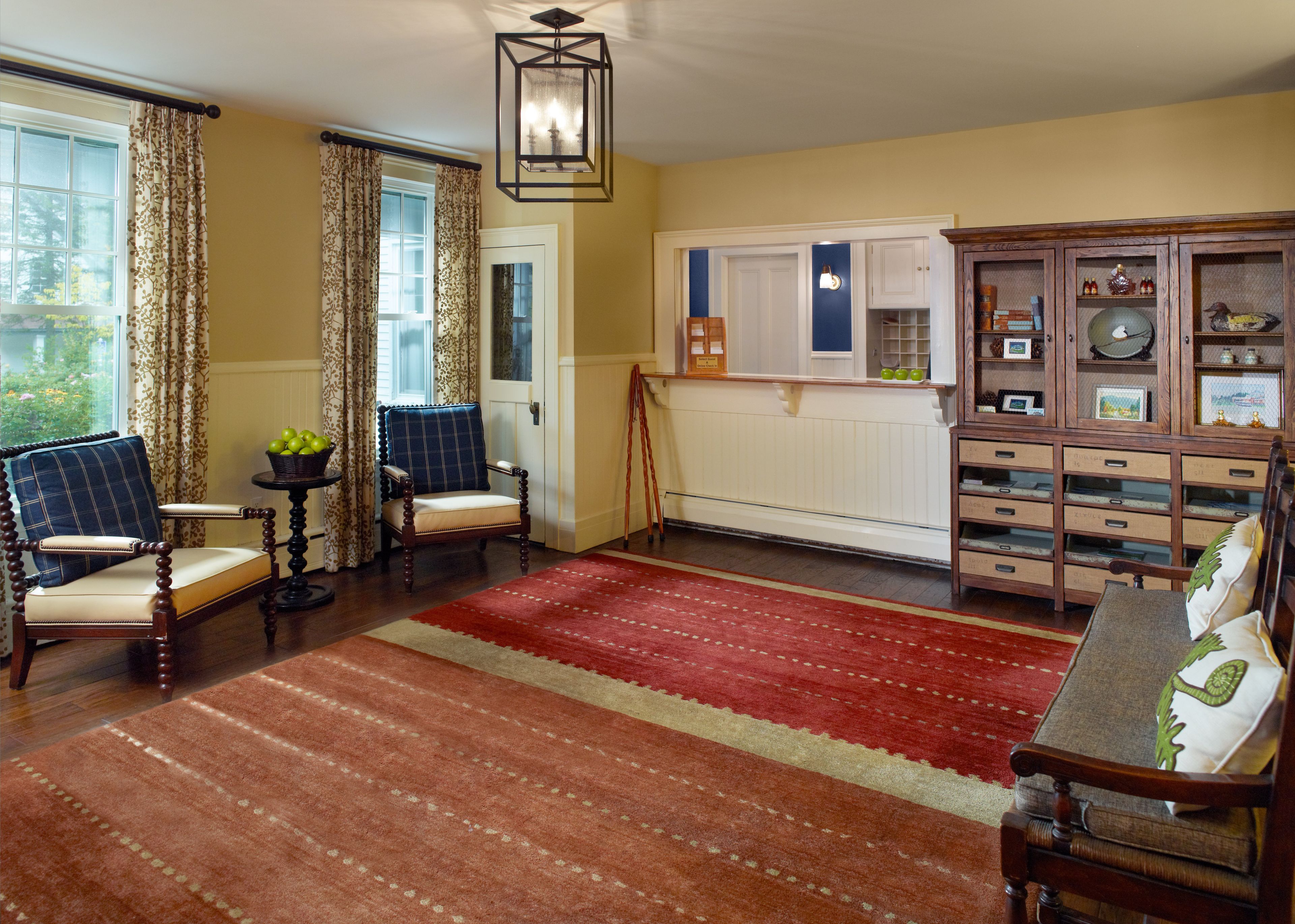 A room with two armchairs, a red patterned rug, a wooden cabinet with drawers, and a window with curtains.