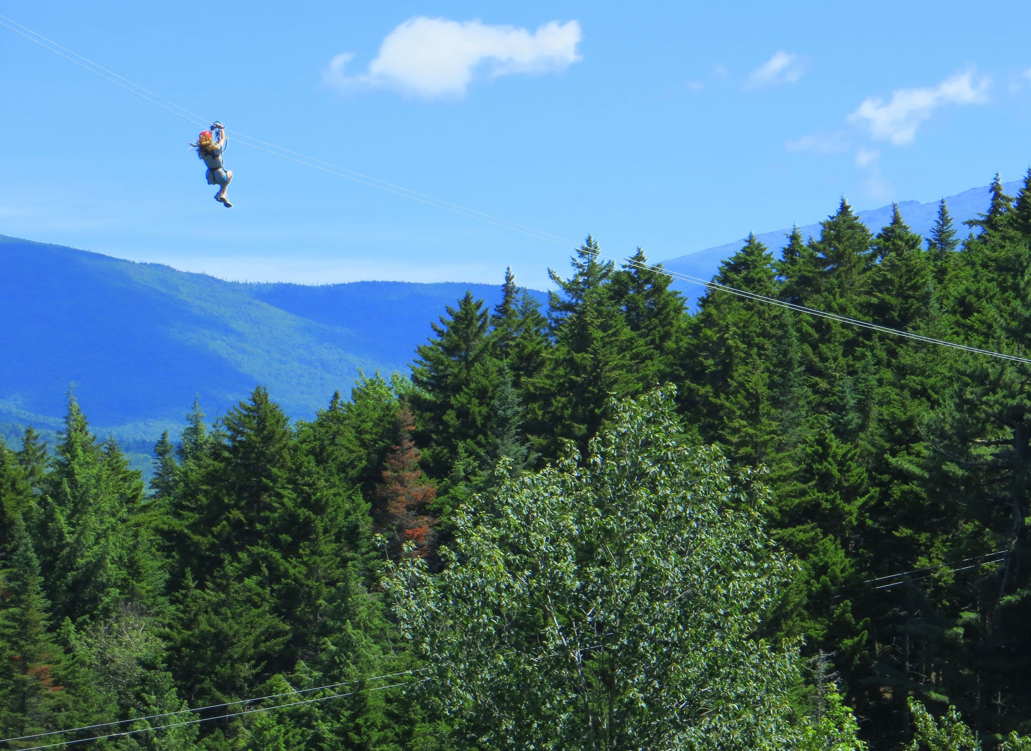 Une personne pratiquant le saut à l’élastique, avec une forêt et des montagnes en arrière-plan.