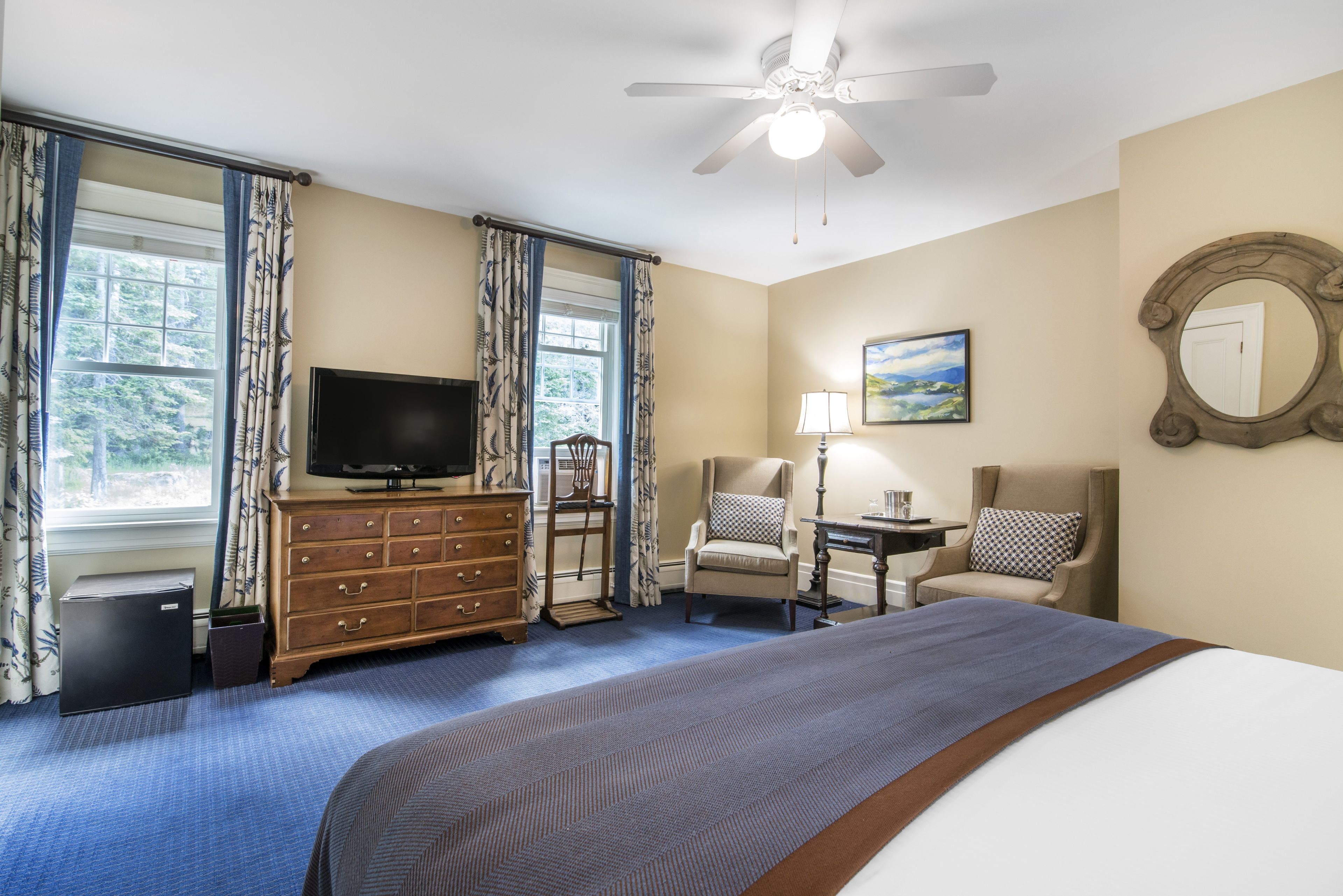 Une chambre d’hôtel équipée d’un lit, d’une télévision, d’un bureau, d’une chaise, d’une lampe et d’un ventilateur de plafond.