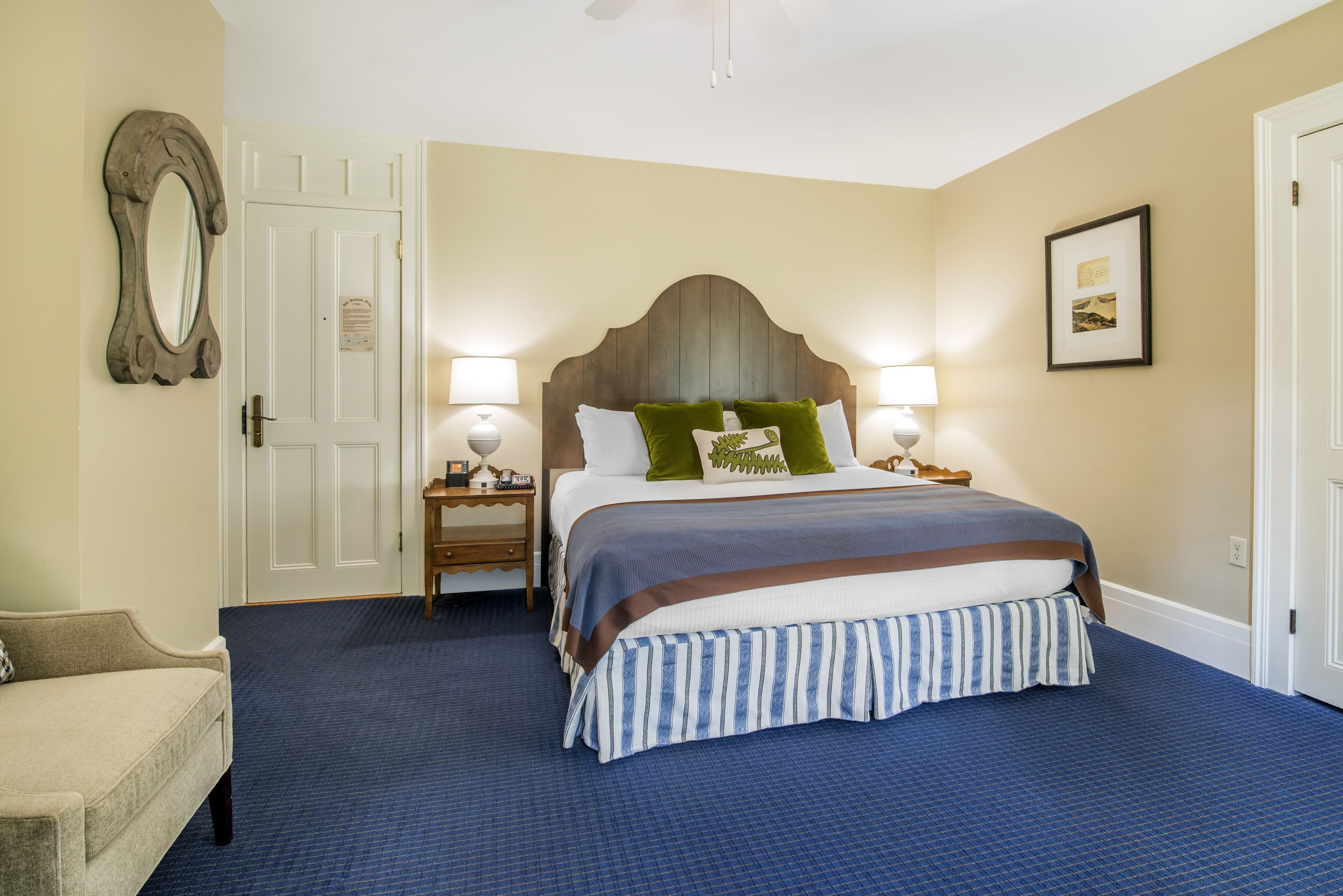 A hotel room with a large bed, two bedside tables with lamps, a chair, and a framed picture on the wall.