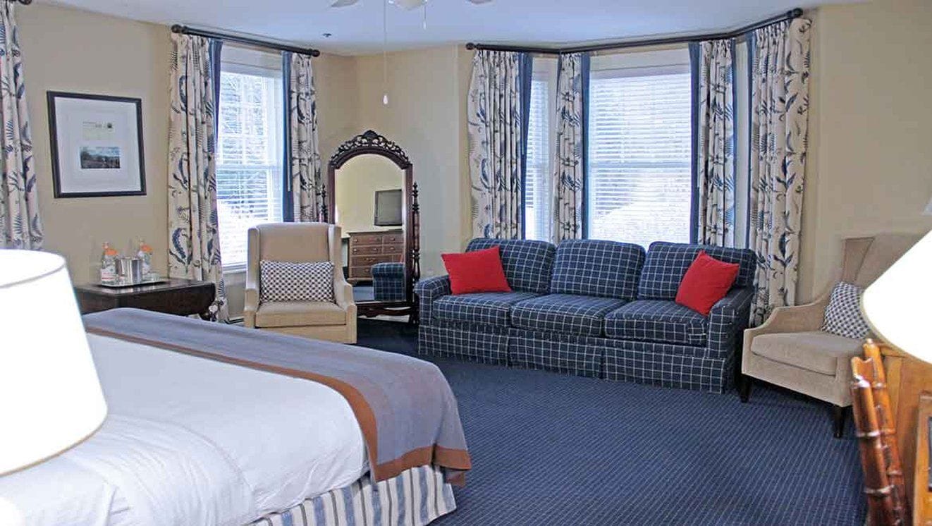 A hotel room with a bed, a sofa, a chair, a desk, a mirror, and curtains.