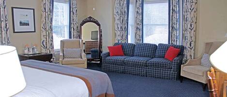 A hotel room with a bed, a sofa, a chair, a desk, a mirror, and curtains.