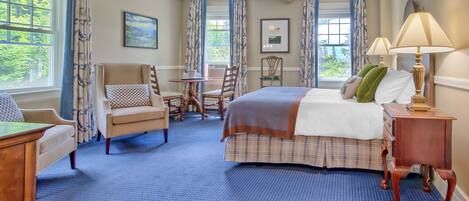A hotel room with a bed, a desk, a chair, a table, and a window with curtains.