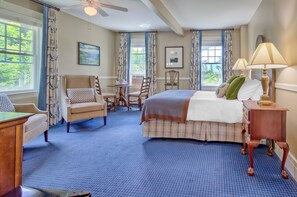 A hotel room with a bed, a desk, a chair, a table, and a window with curtains.