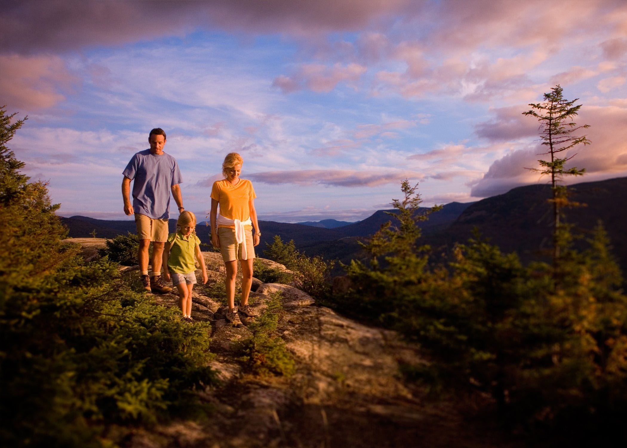 A family walking on a rocky path with a mountainous landscape in the background.