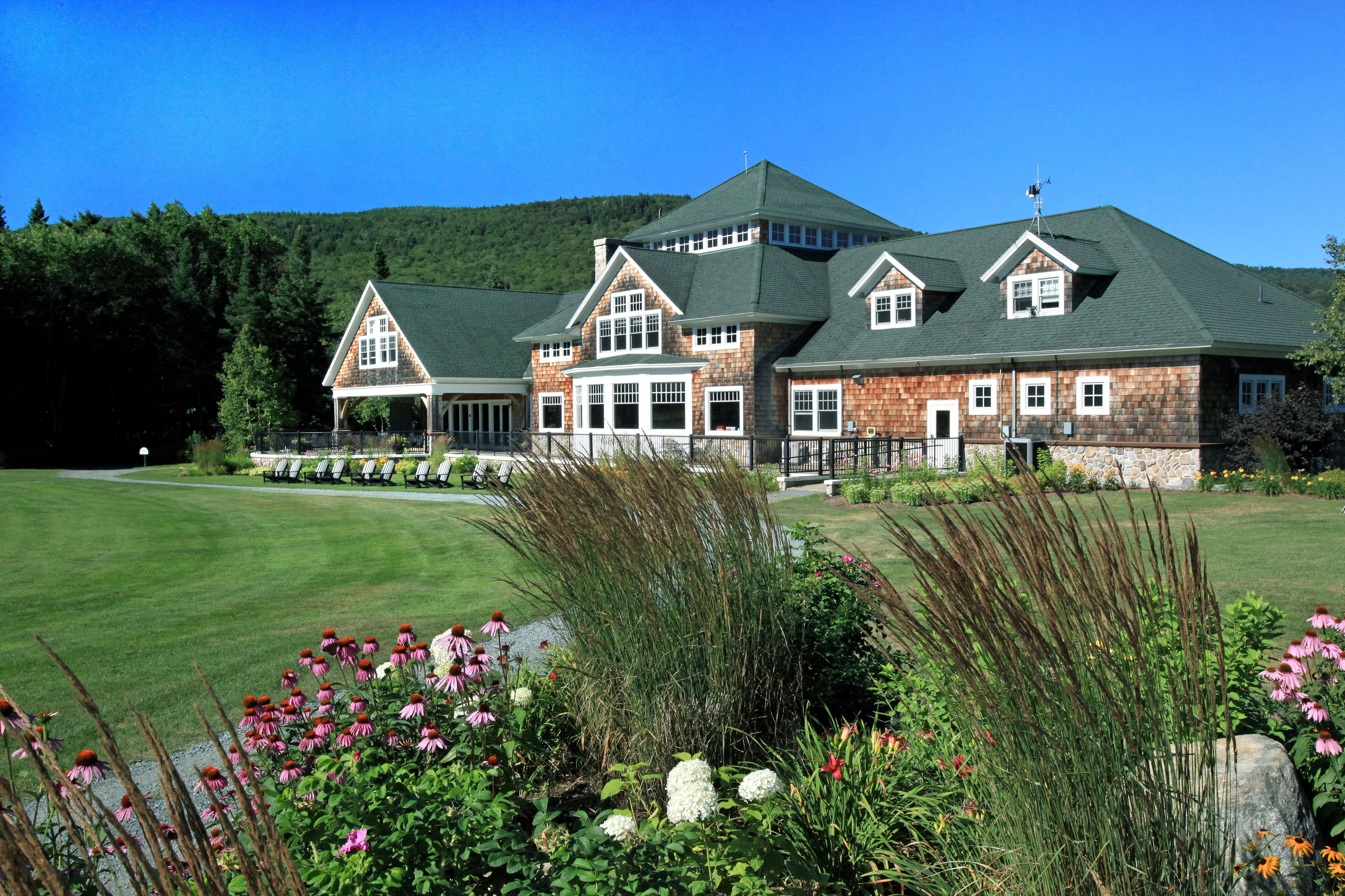 A large, multi-story building with a green roof, surrounded by a well-maintained lawn and various flowering plants.