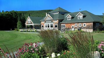 A large, multi-story building with a green roof, surrounded by a well-maintained lawn and various flowering plants.