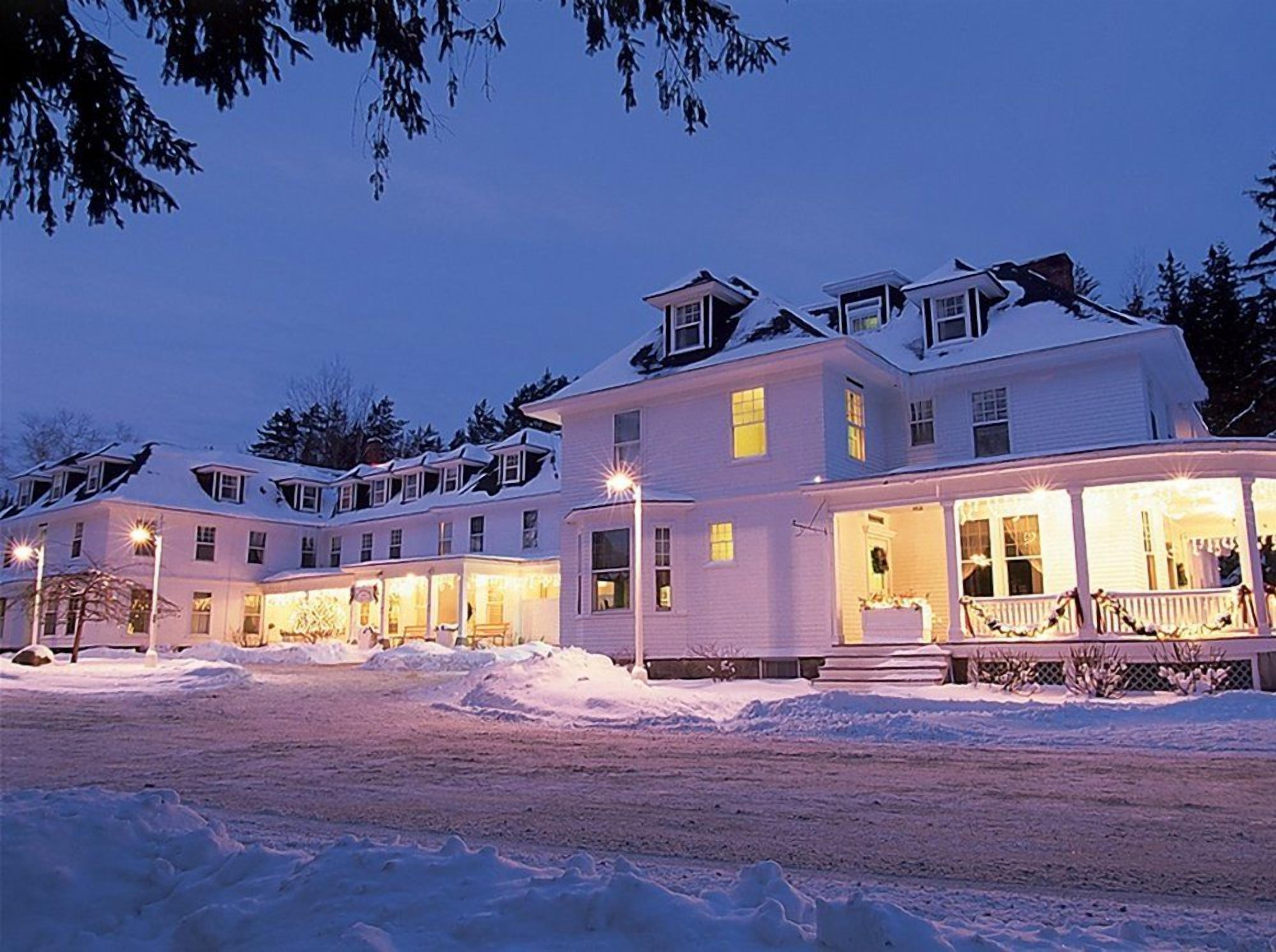 A large, multi-story building with a snow-covered roof and illuminated windows, surrounded by snow.