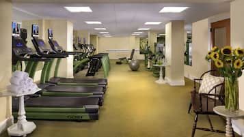Une salle de sport équipée de tapis de course, de ballons d’exercice et d’une chaise sur laquelle est posé un vase rempli de tournesols.