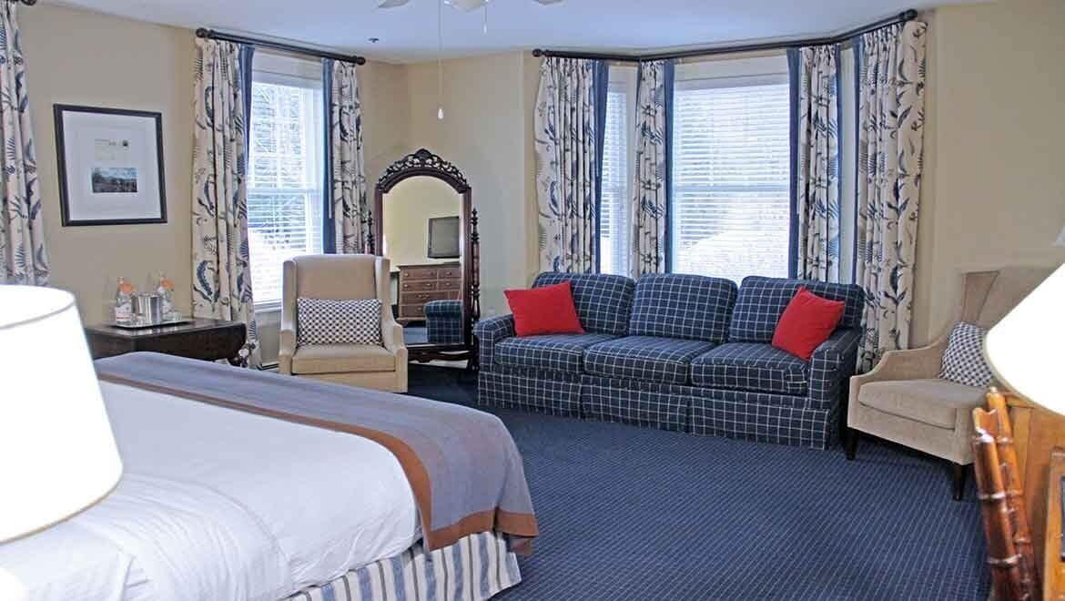 A hotel room with a bed, a sofa, a chair, a desk, and a mirror.
