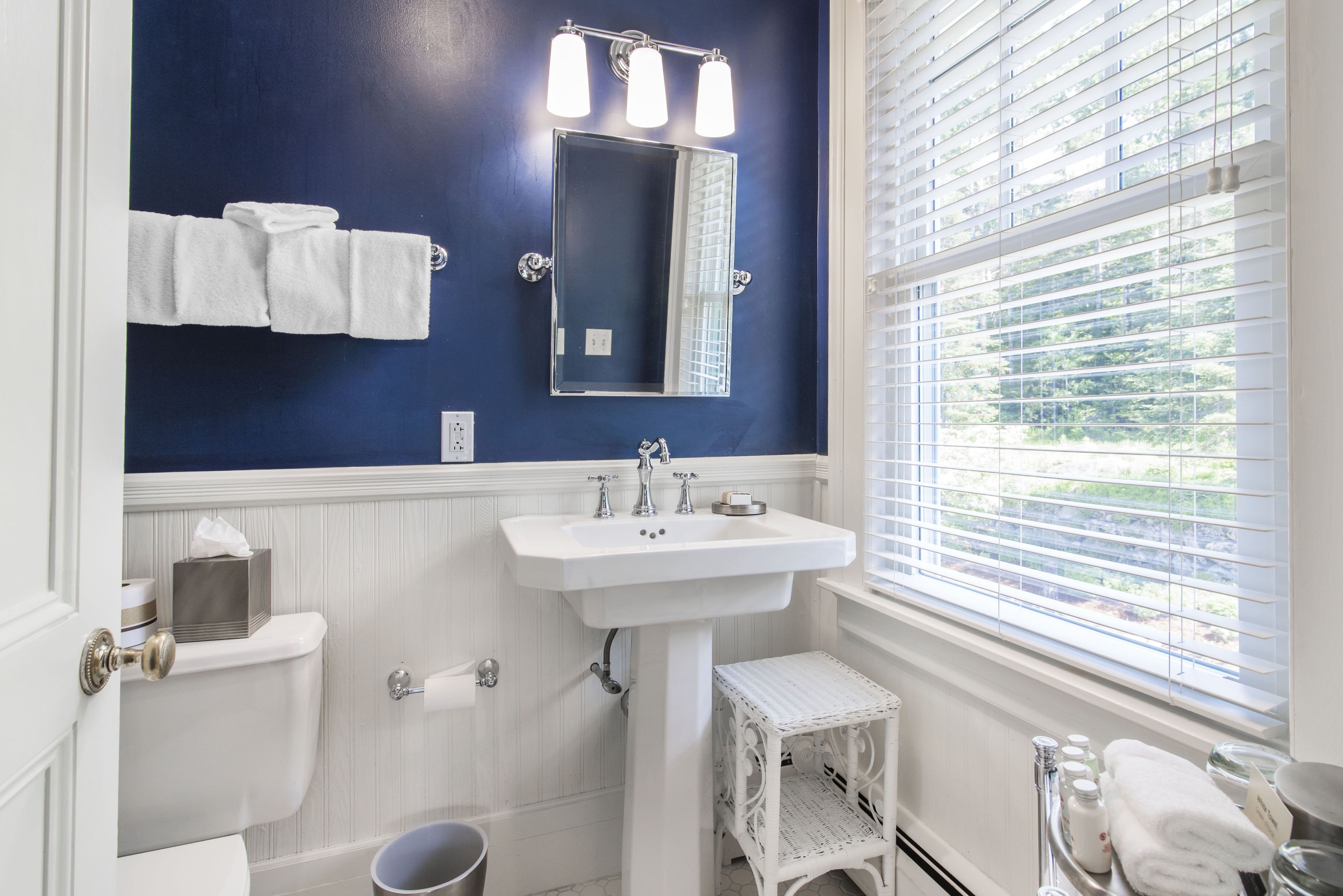 A bathroom with a white sink, a mirror, and a window with blinds.