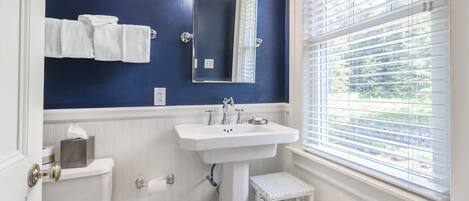 A bathroom with a white sink, a mirror, and a window with blinds.