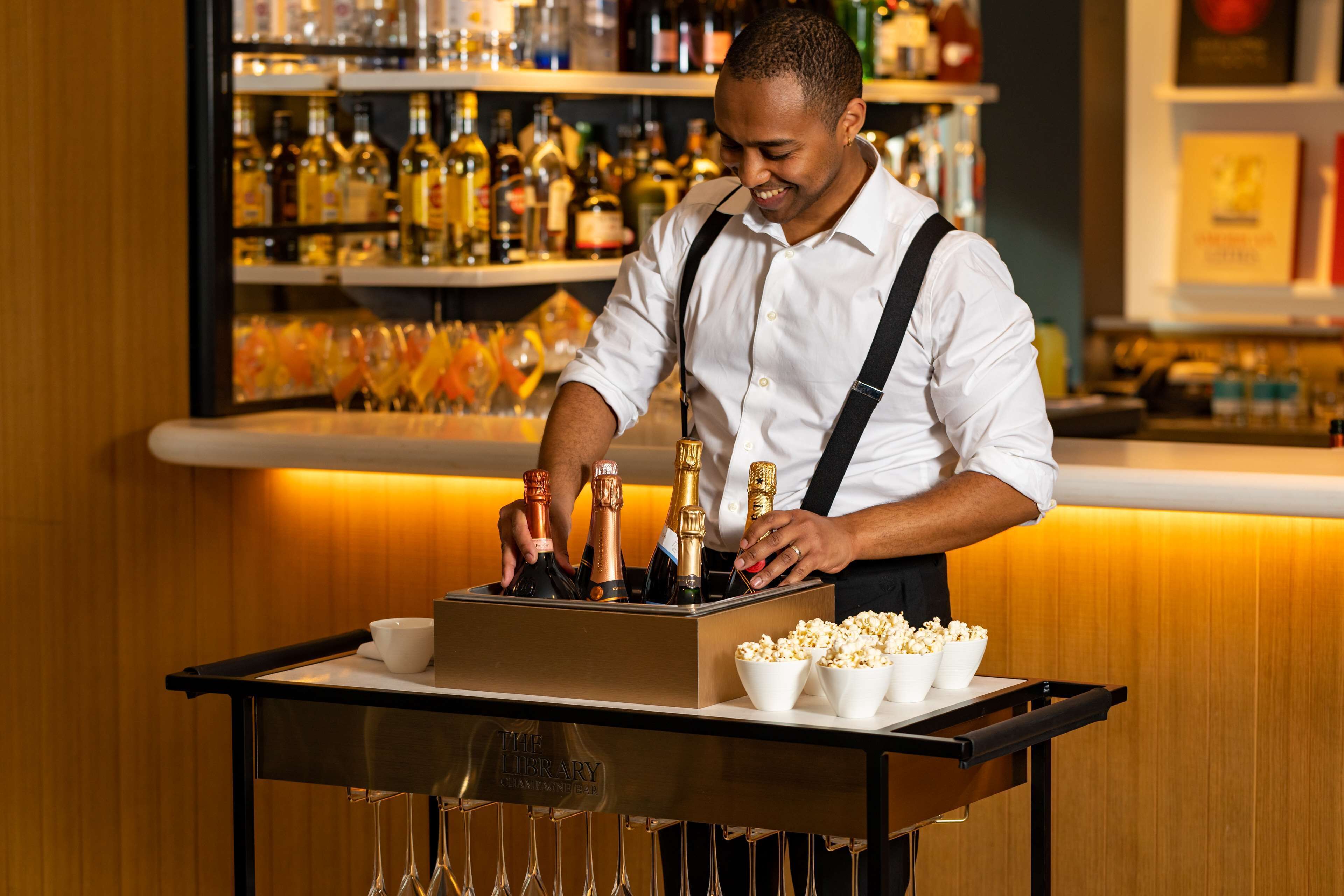 A bartender at a bar with a tray of drinks and glasses.