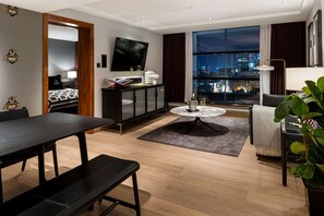 A modern hotel room with a city view, a flat-screen TV, a dining area, and a cozy seating space.