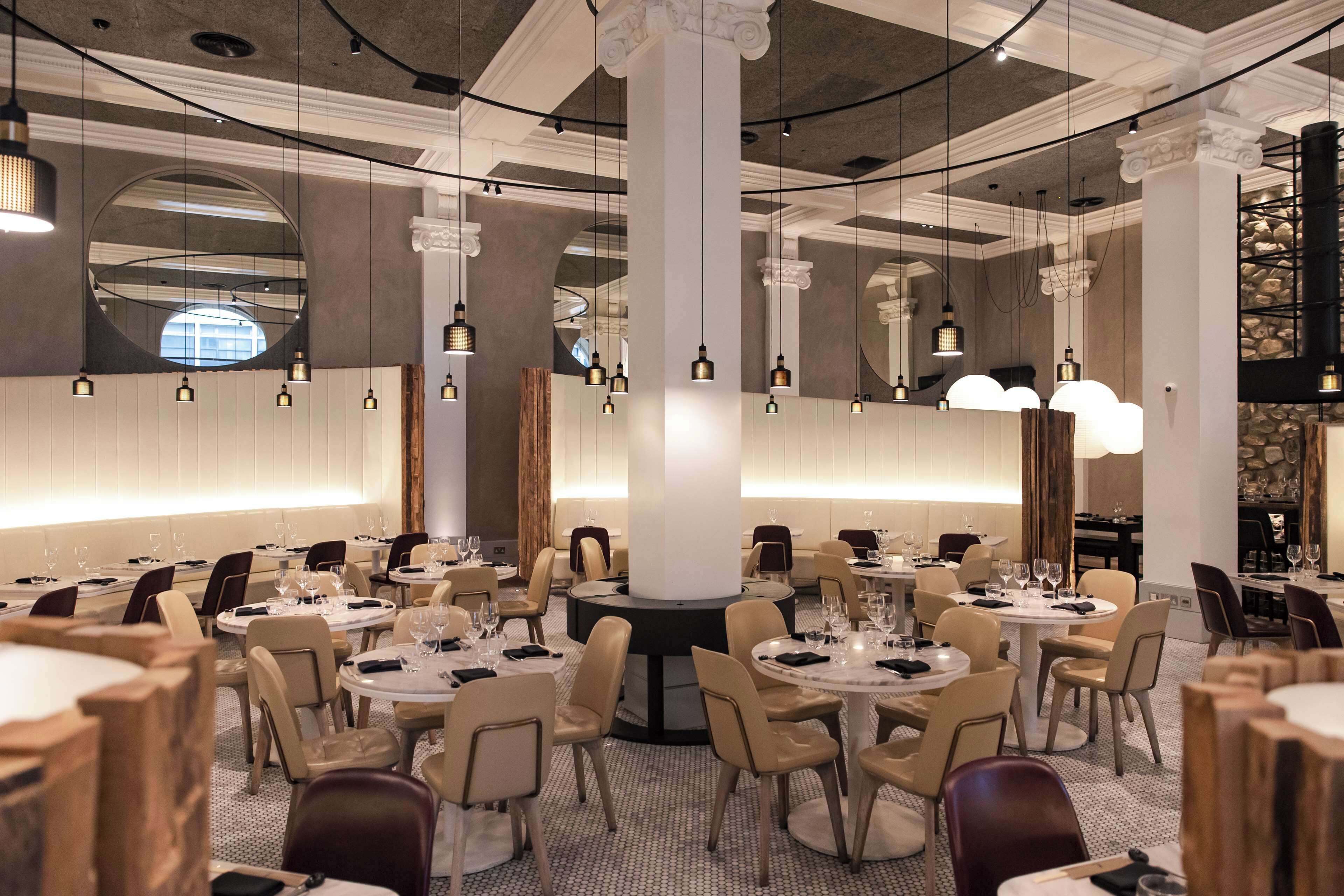 A spacious dining area with round tables and chairs, large columns, and hanging pendant lights.