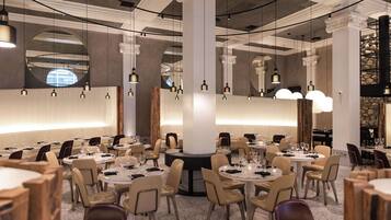A spacious dining area with round tables and chairs, large columns, and hanging pendant lights.