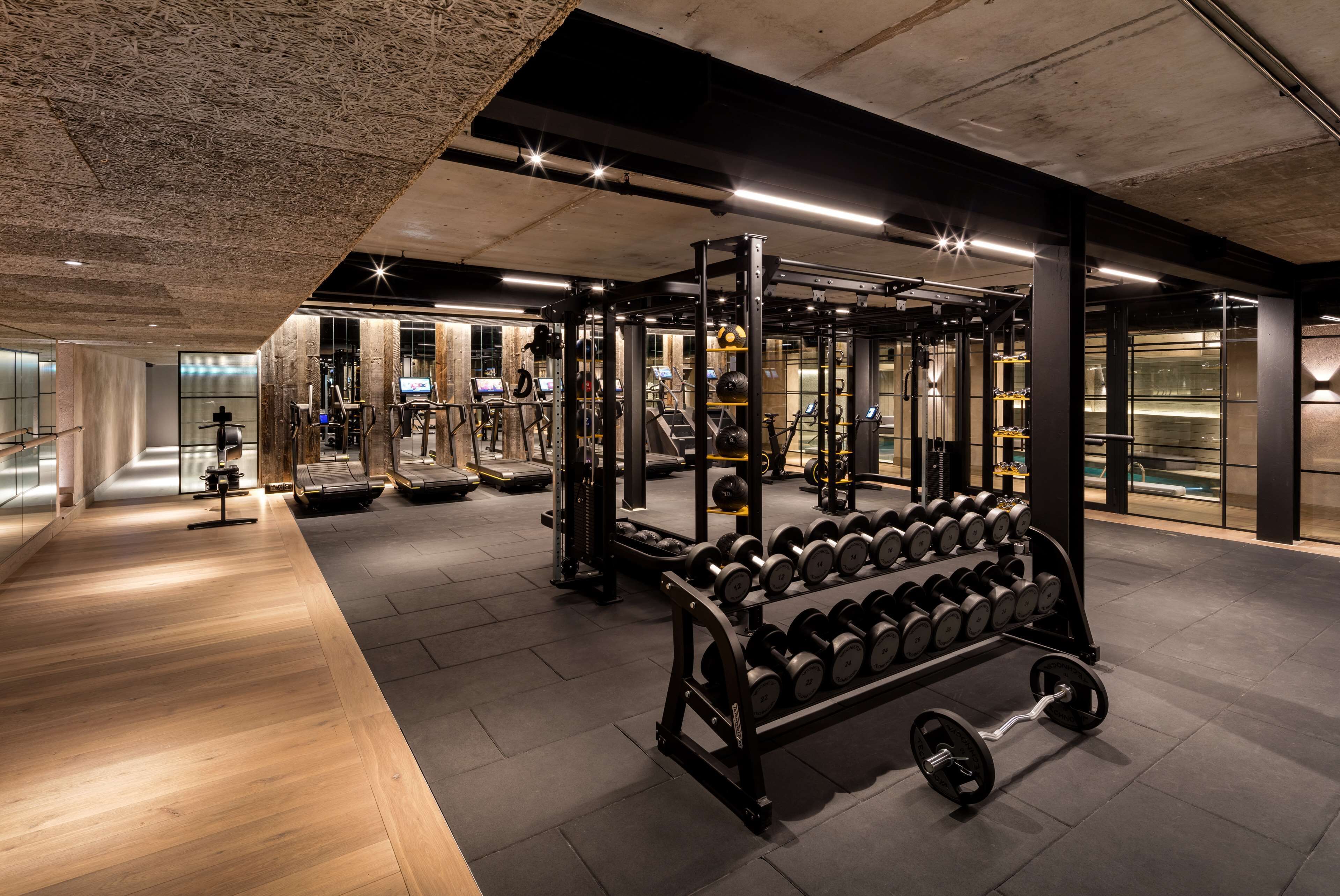 A modern gym with various weightlifting equipment, treadmills, and a rack of dumbbells.