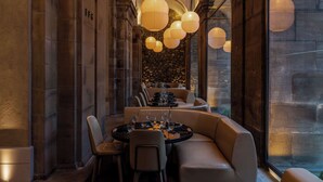 A dimly lit dining area with round tables and leather seating, stone walls, and hanging paper lanterns.