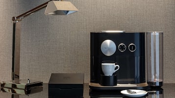 Una cafetera moderna con un porta-tazas, una cuchara y una caja, todo sobre una superficie reflectante.