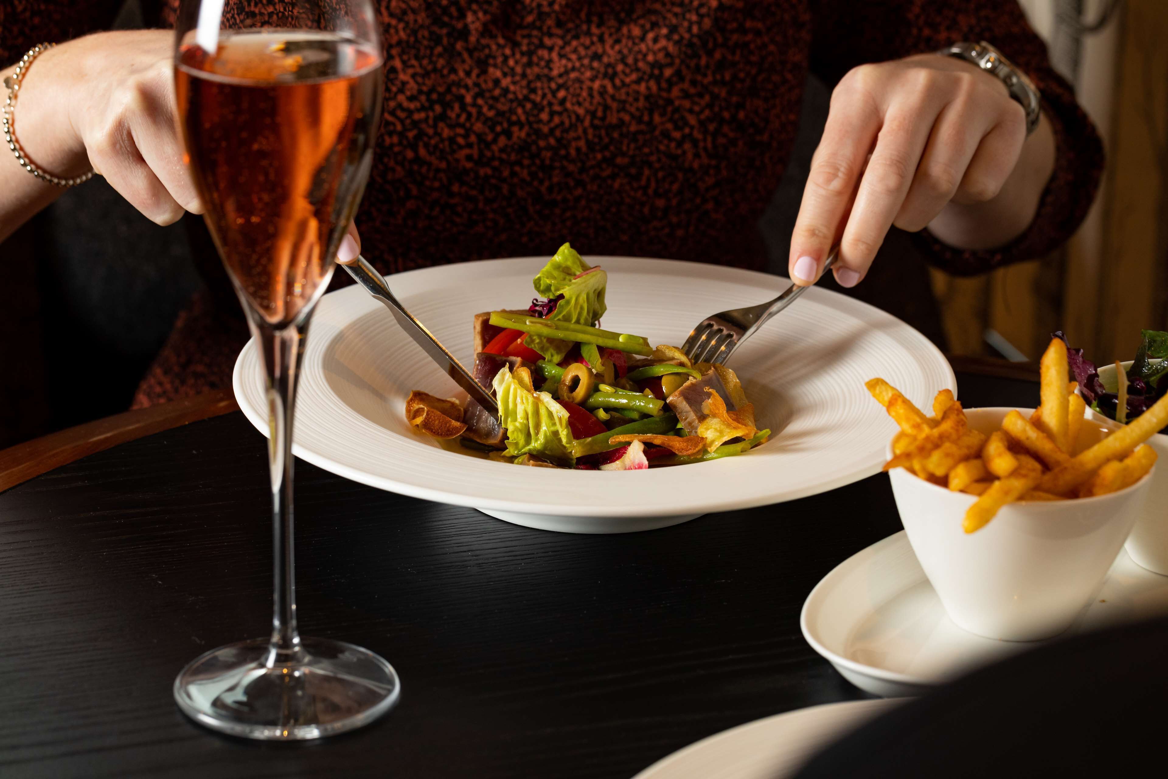 A person dining with a plate of food and a glass of drink on a table.