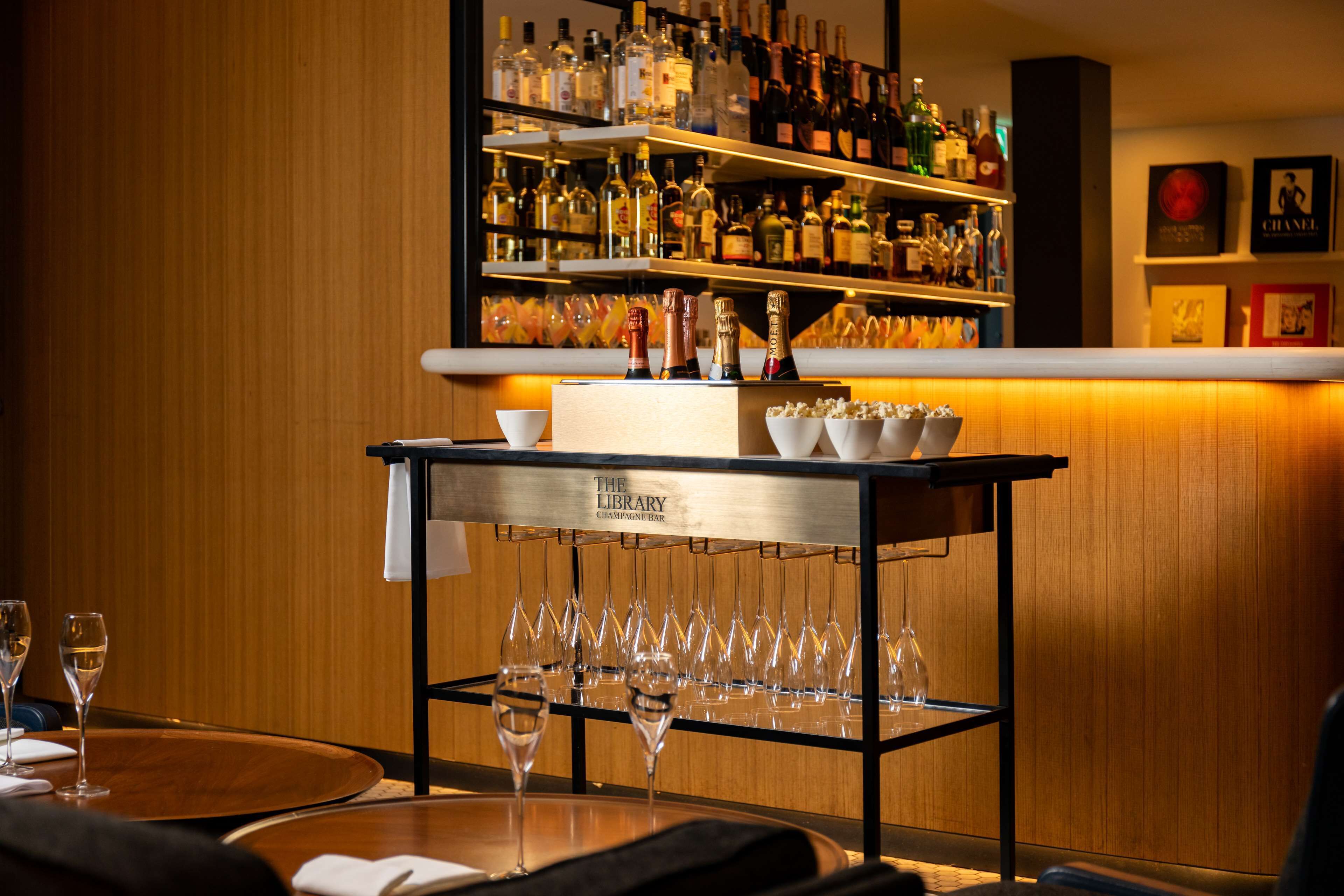 A bar area with shelves of liquor bottles, a bar cart with glasses, and a wine glass on a table.