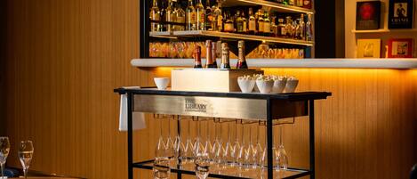 A bar area with shelves of liquor bottles, a bar cart with glasses, and a wine glass on a table.