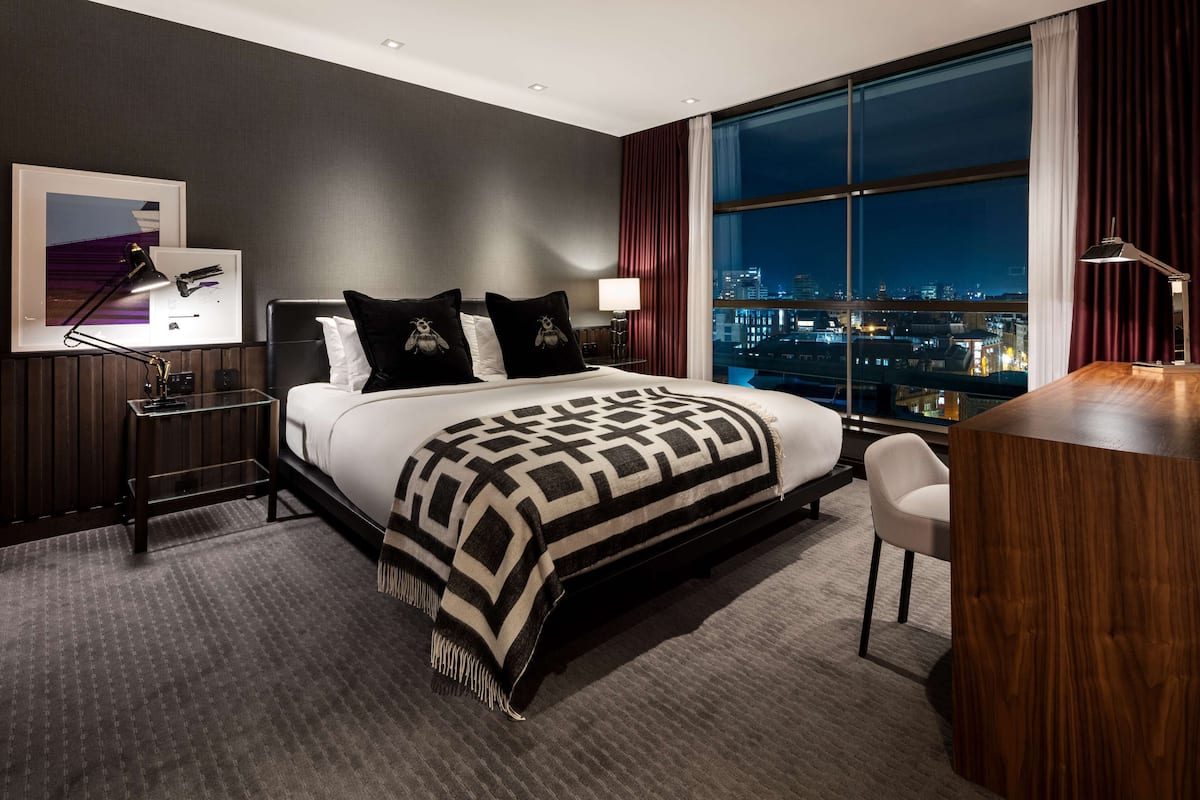 A modern hotel room with a large bed, a desk, and a city view.