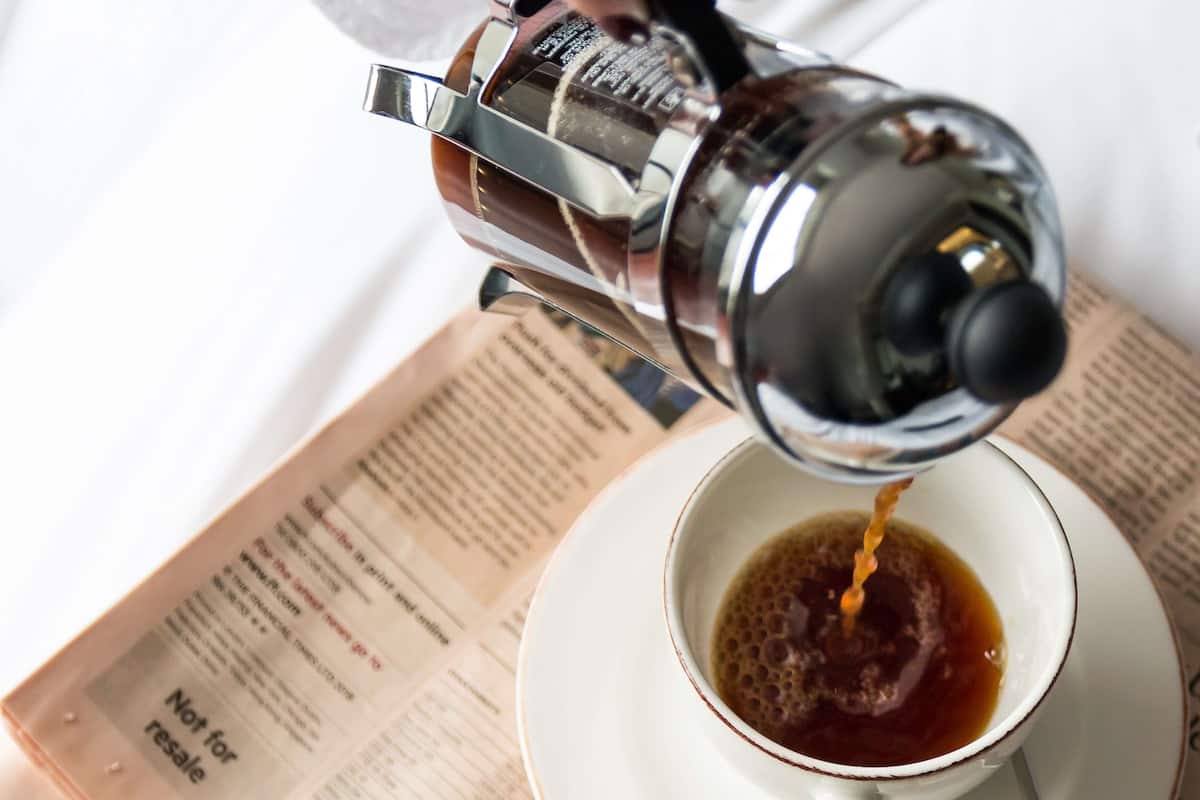 A coffee pot pouring coffee into a cup on a newspaper.