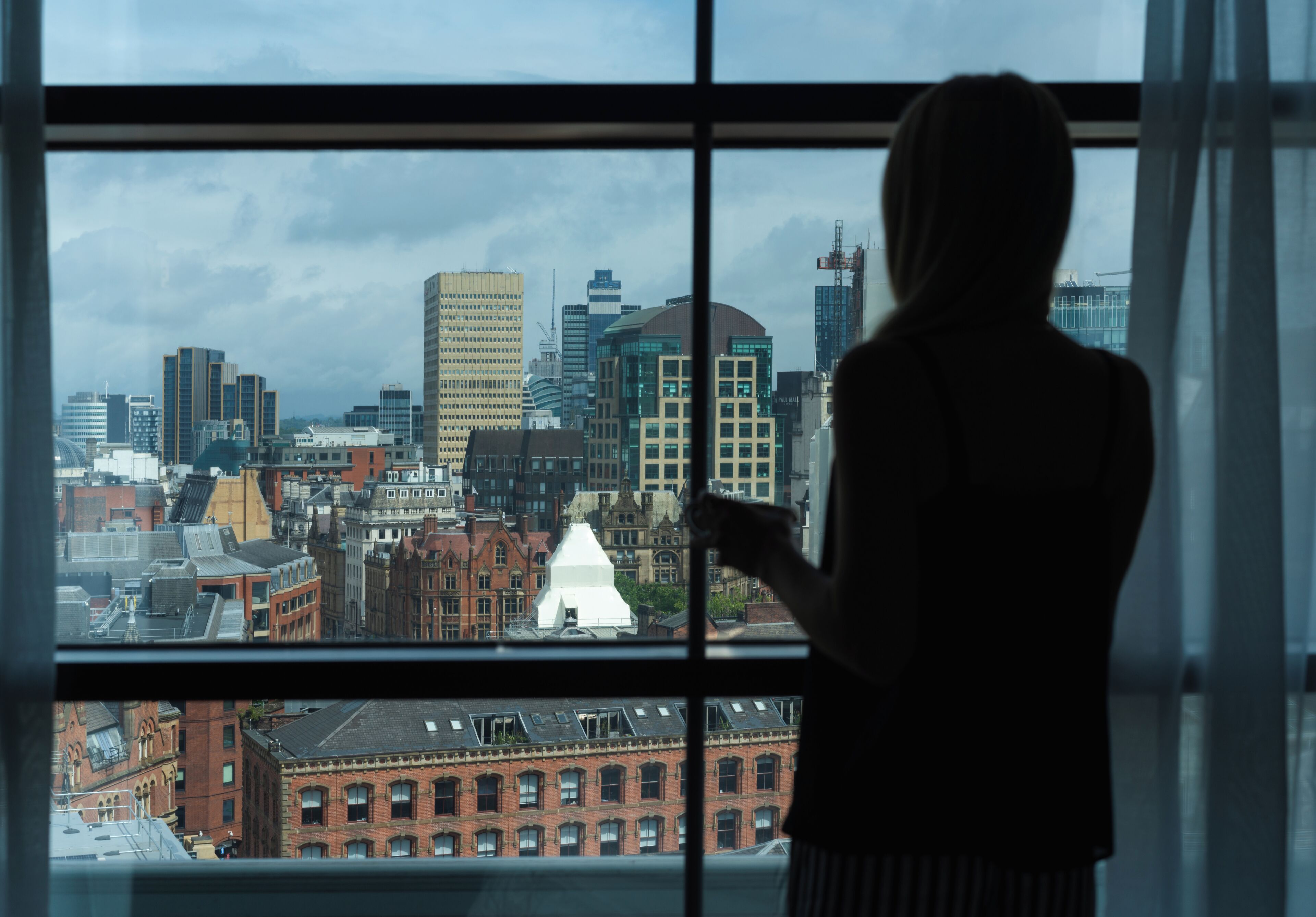 Una persona de pie junto a una ventana con vistas a un paisaje urbano.