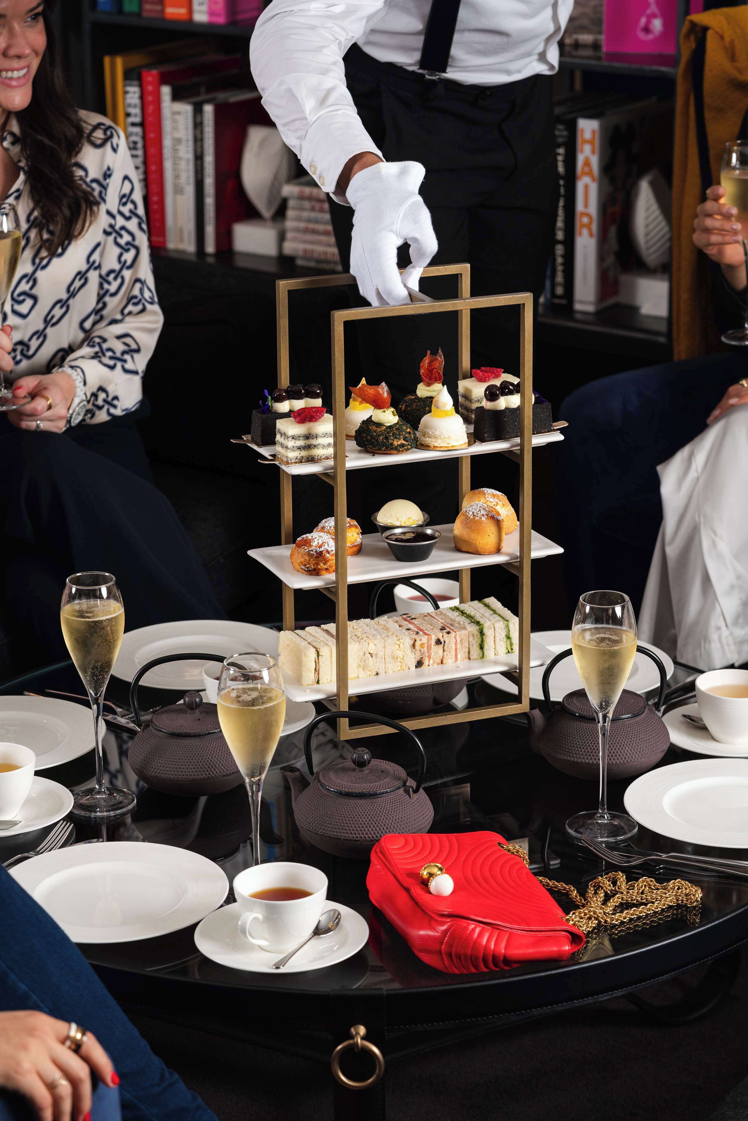 Une présentation de desserts à plusieurs niveaux, avec divers pâtisseries, et un sac à main rouge posé sur une table.