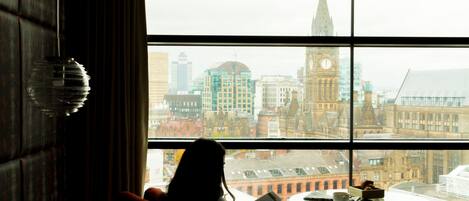 A person reading a book by a window with a view of a cityscape including a clock tower.