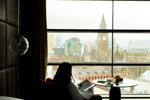 Guests can enjoy a city view from the large window, featuring a prominent clock tower, while relaxing in the room.