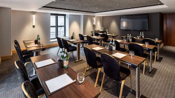 A conference room with multiple tables, chairs, and a large flat-screen TV.