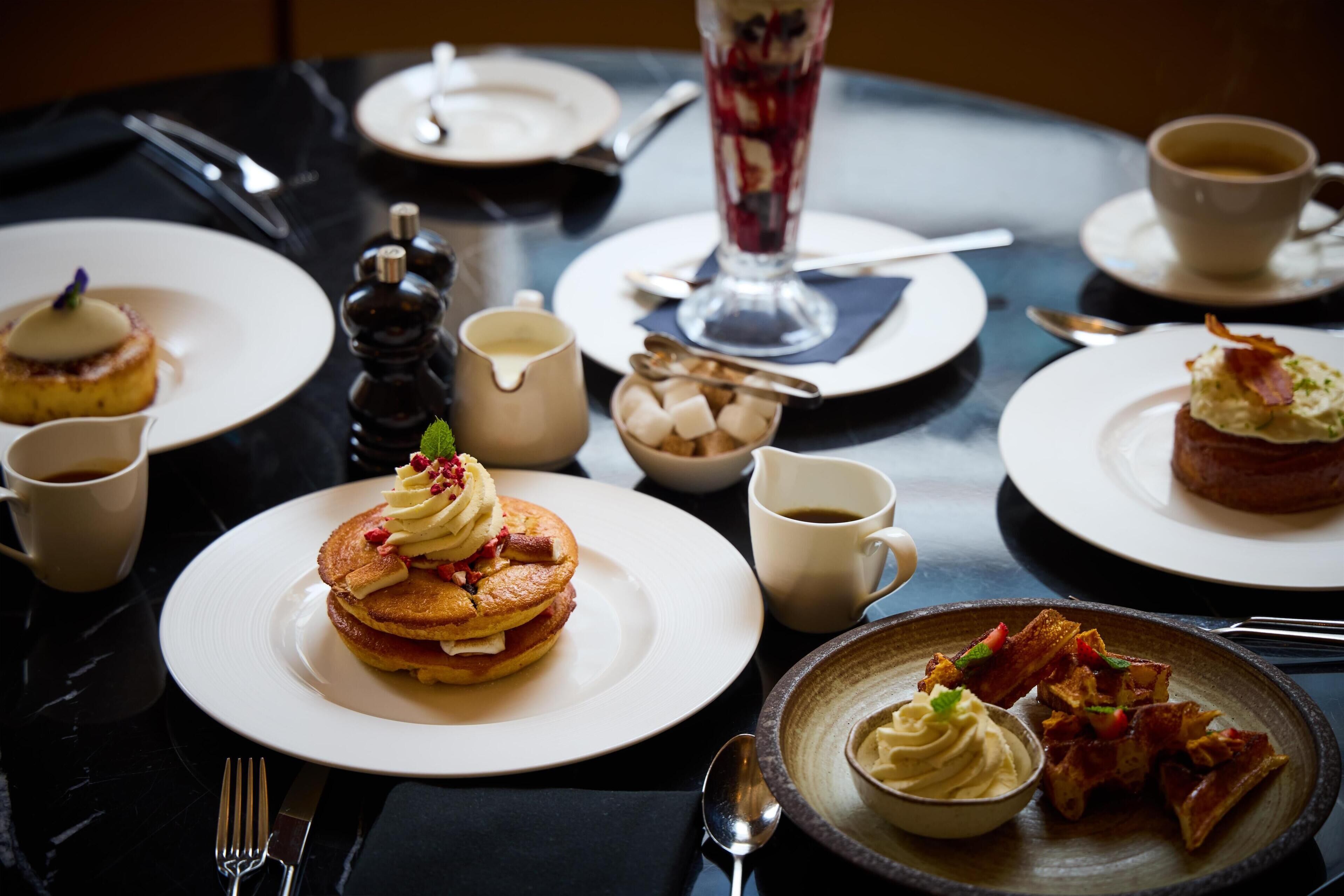 A dining table with various breakfast dishes, including pancakes, waffles, and a dessert.