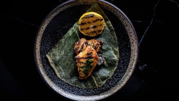 A plate with grilled chicken and a grilled lemon half on a dark speckled plate.