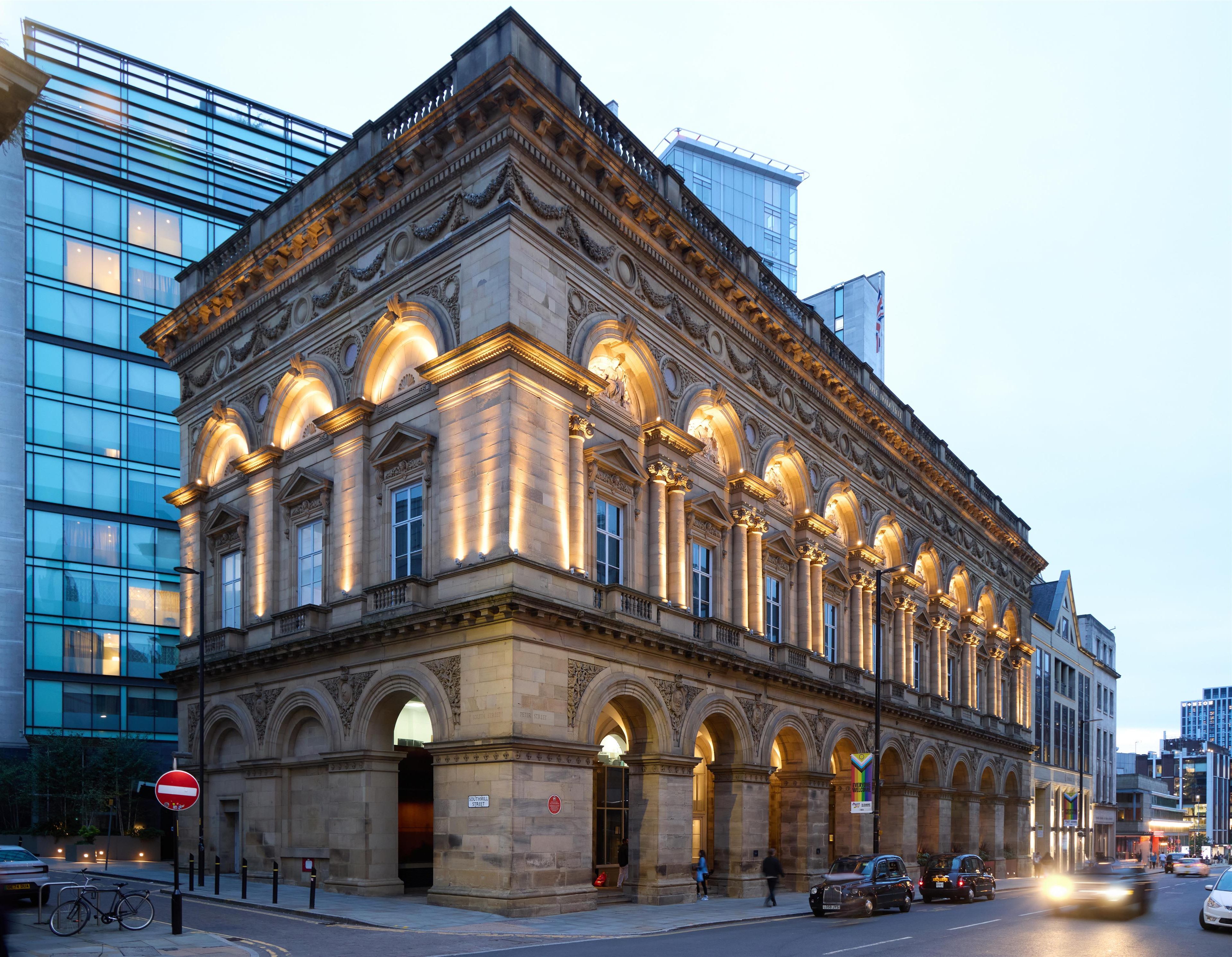 A historic building with classical architecture, featuring a series of arches and columns, and a modern glass building adjacent to it.