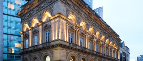A historic building with classical architecture, featuring a series of arches and columns, and a modern glass building adjacent to it.