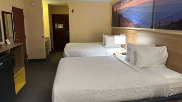A hotel room with two beds, a desk with a lamp, a painting of a mountain landscape, and a door leading to another room.