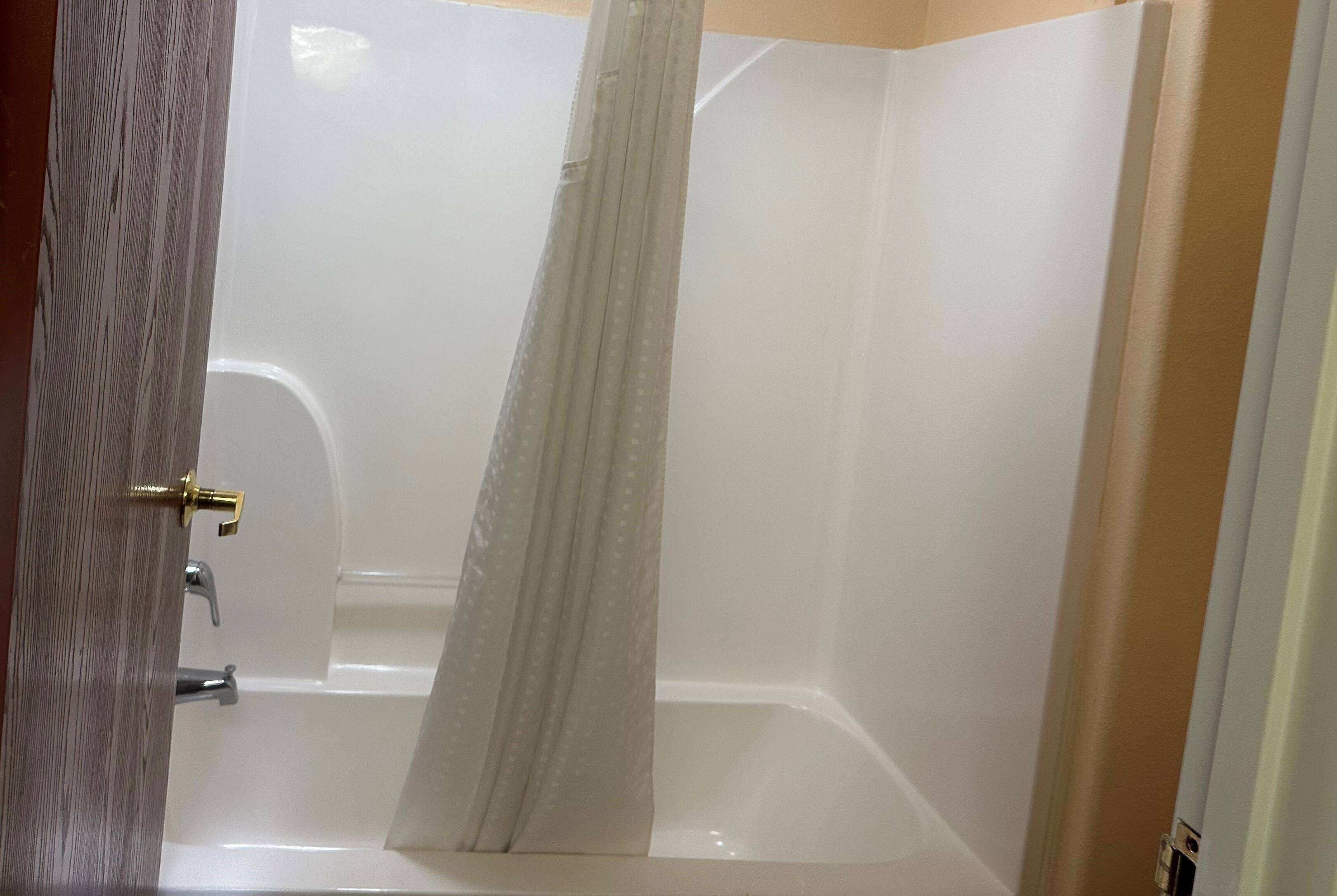 Un baño con bañera, cortina de ducha y una puerta con tirador de latón.