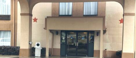 Una entrada de edificio con puerta de cristal, dos ventanas con cortinas y una decoración con forma de estrella en la pared.
