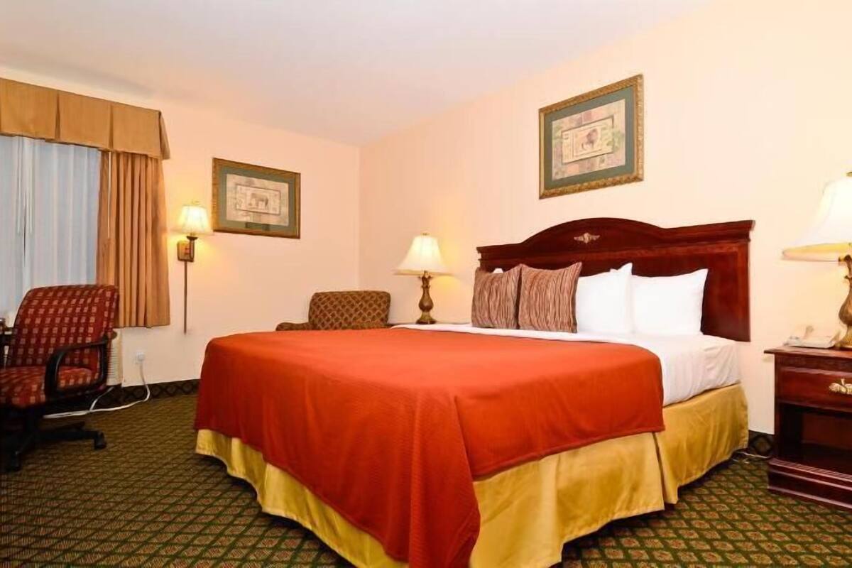 A hotel room with a large bed, two bedside lamps, a chair, a desk, and a framed picture on the wall.