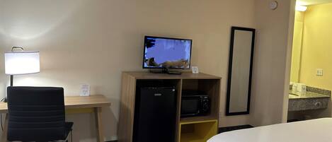 Hotelkamer met een bed, bureau met computer, koelkast, magnetron, lamp en spiegel.